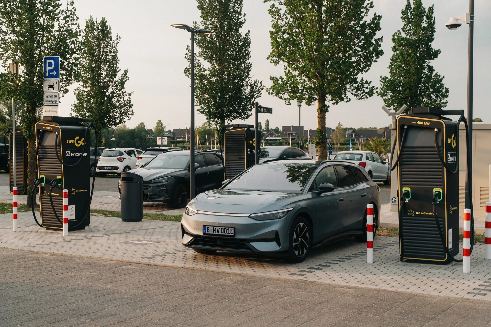 Mehrere Ladesäulen stehen auf einem Parkplatz. Graues E-Auto an einer schwarzen Schnellladesäule mit 400 Kilowatt Leistung. Mehrere Ladesäulen stehen auf einem Parkplatz. Ein Parkschild weist auf Ladeplätze hin.Graues E-Auto an einer schwarzen Schnellladesäule von EWE Go mit 400 Kilowatt Leistung.