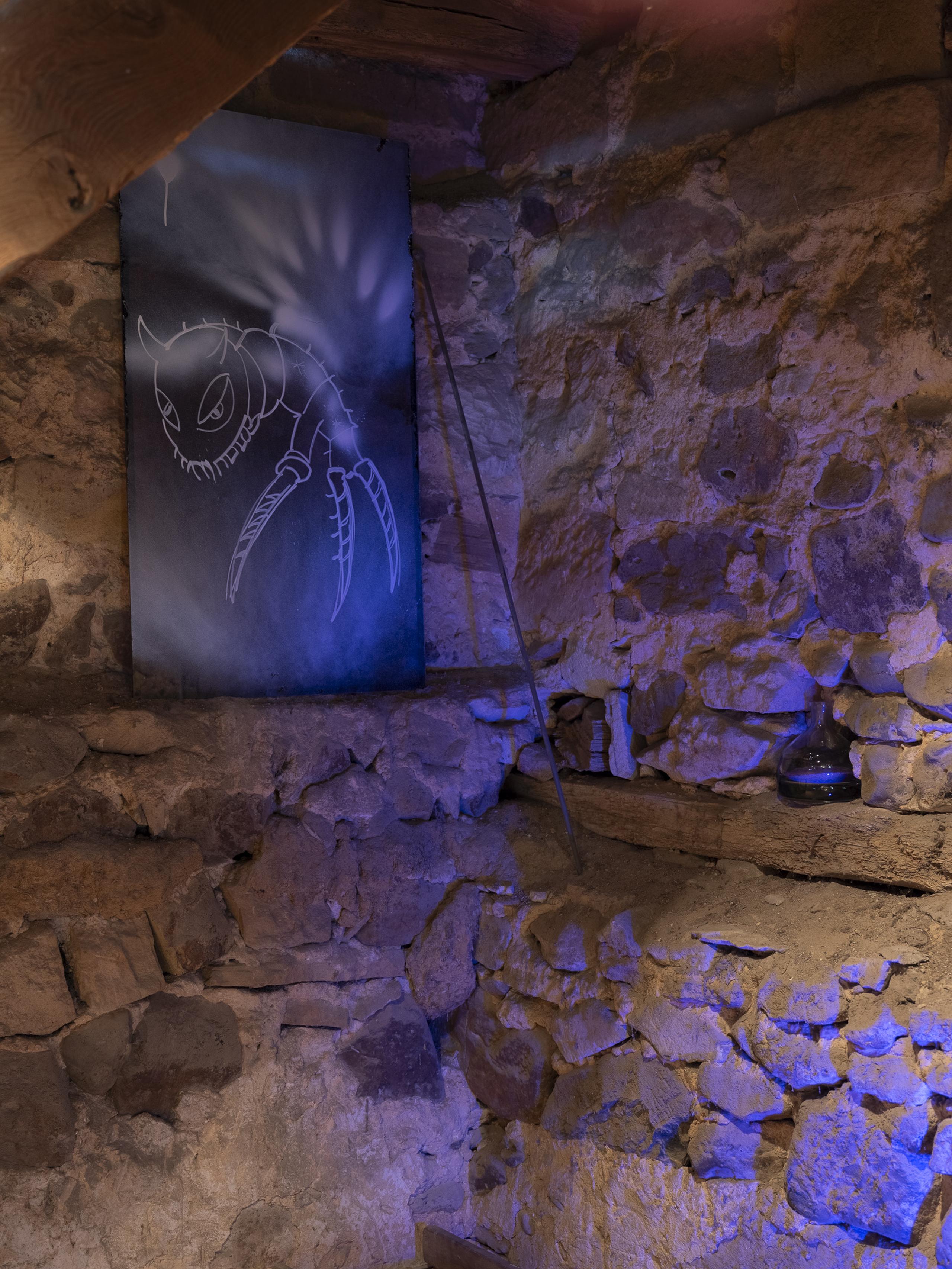 Stone wall with blue lighting, featuring a painting of an insect-like creature. A shelf holds a small bottle and other items.