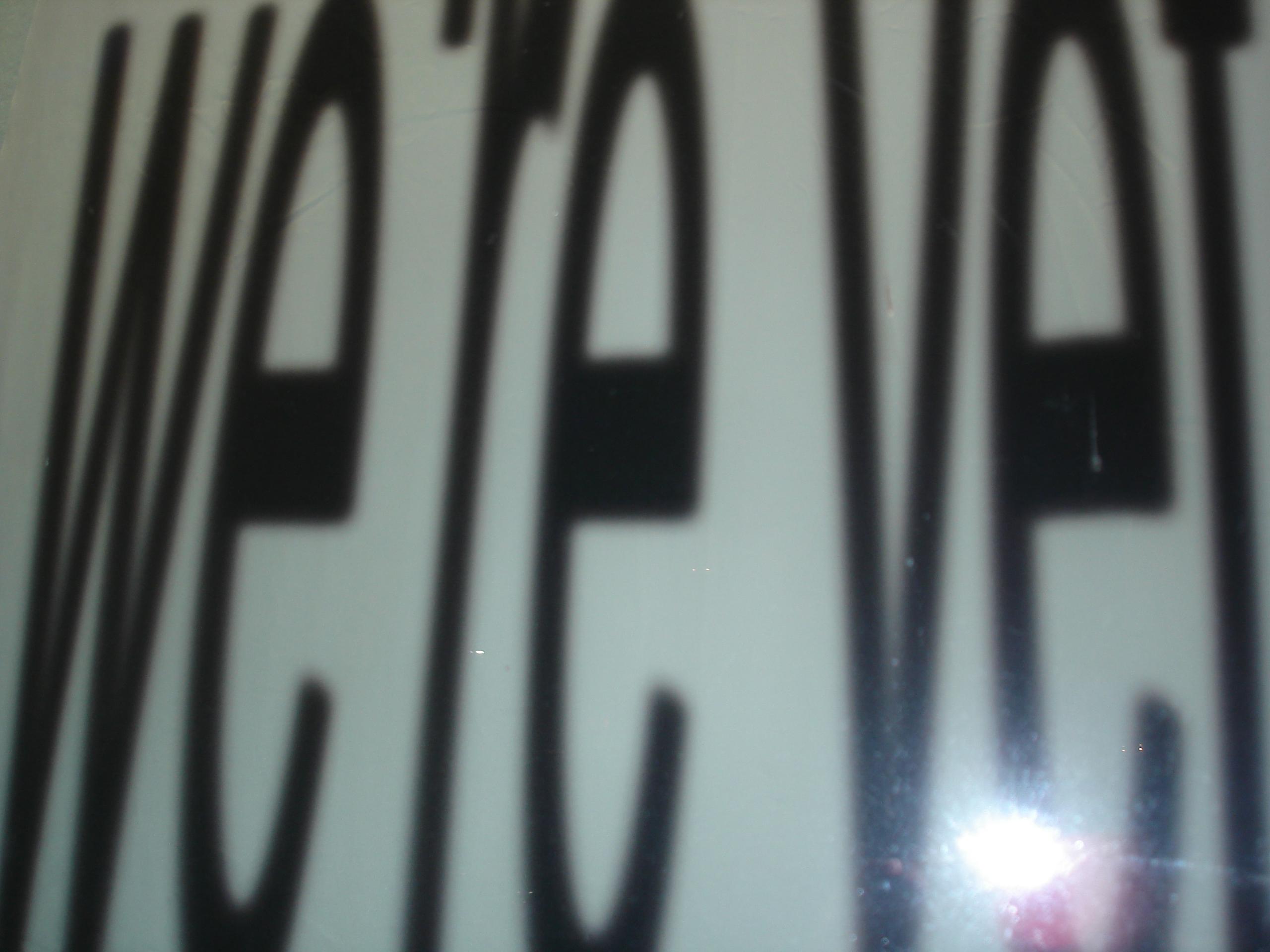 Blurry text in large black letters, partially visible on a white background with a glare reflecting in the corner.