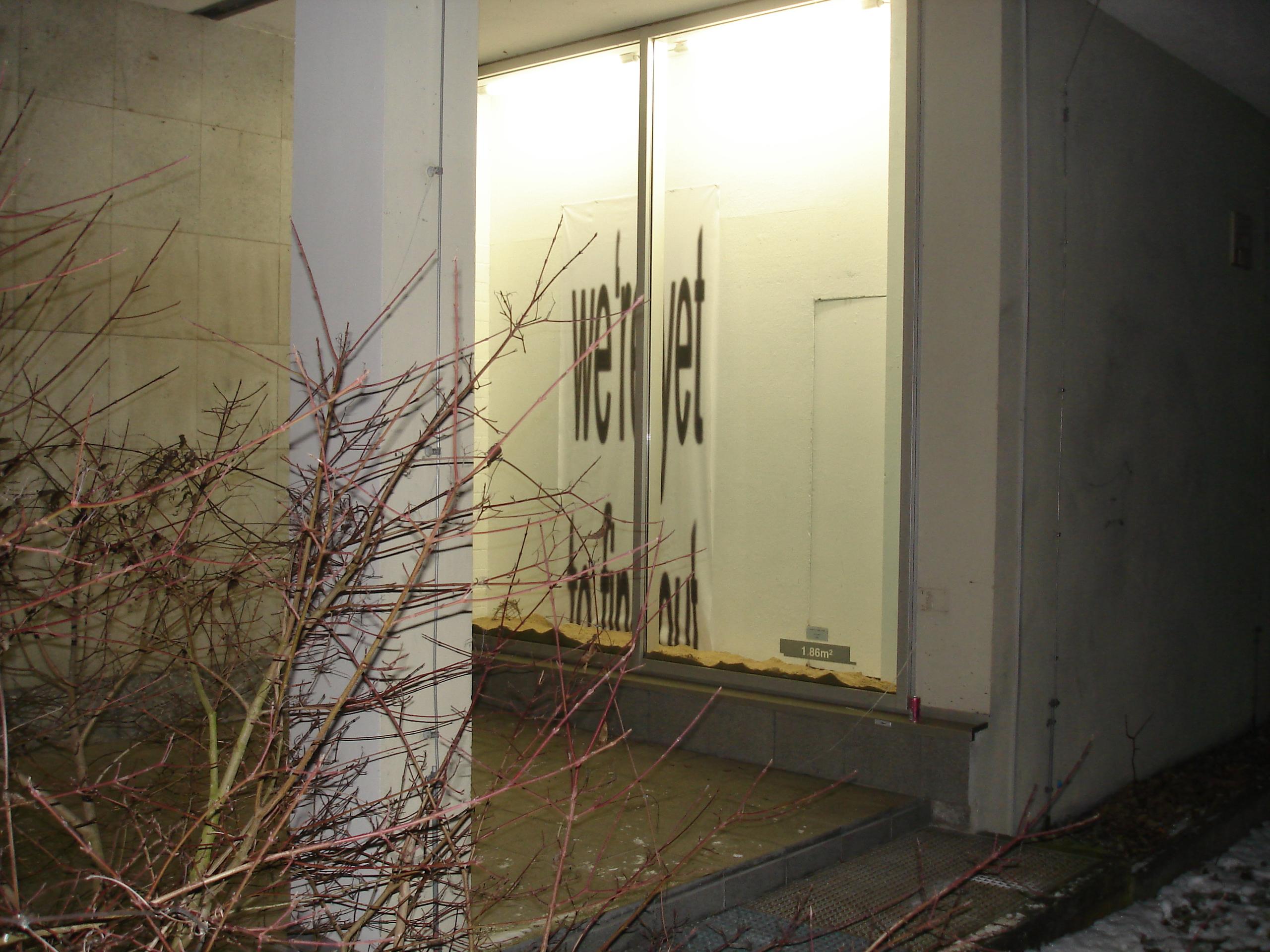 Empty storefront with large windows displaying reversed text; barren plants in the foreground.