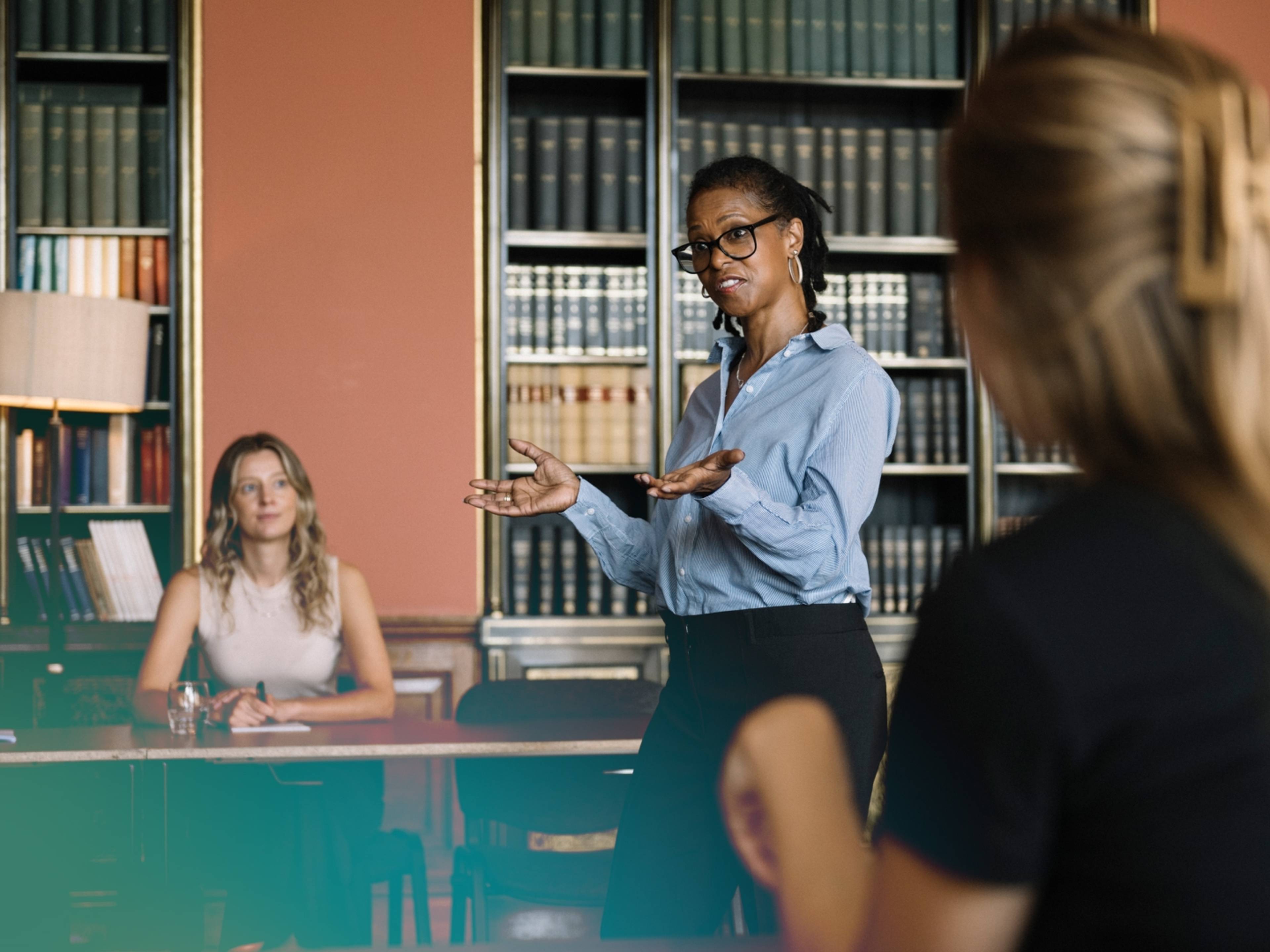A business leader speaks confidently to her team in a library corporate setting