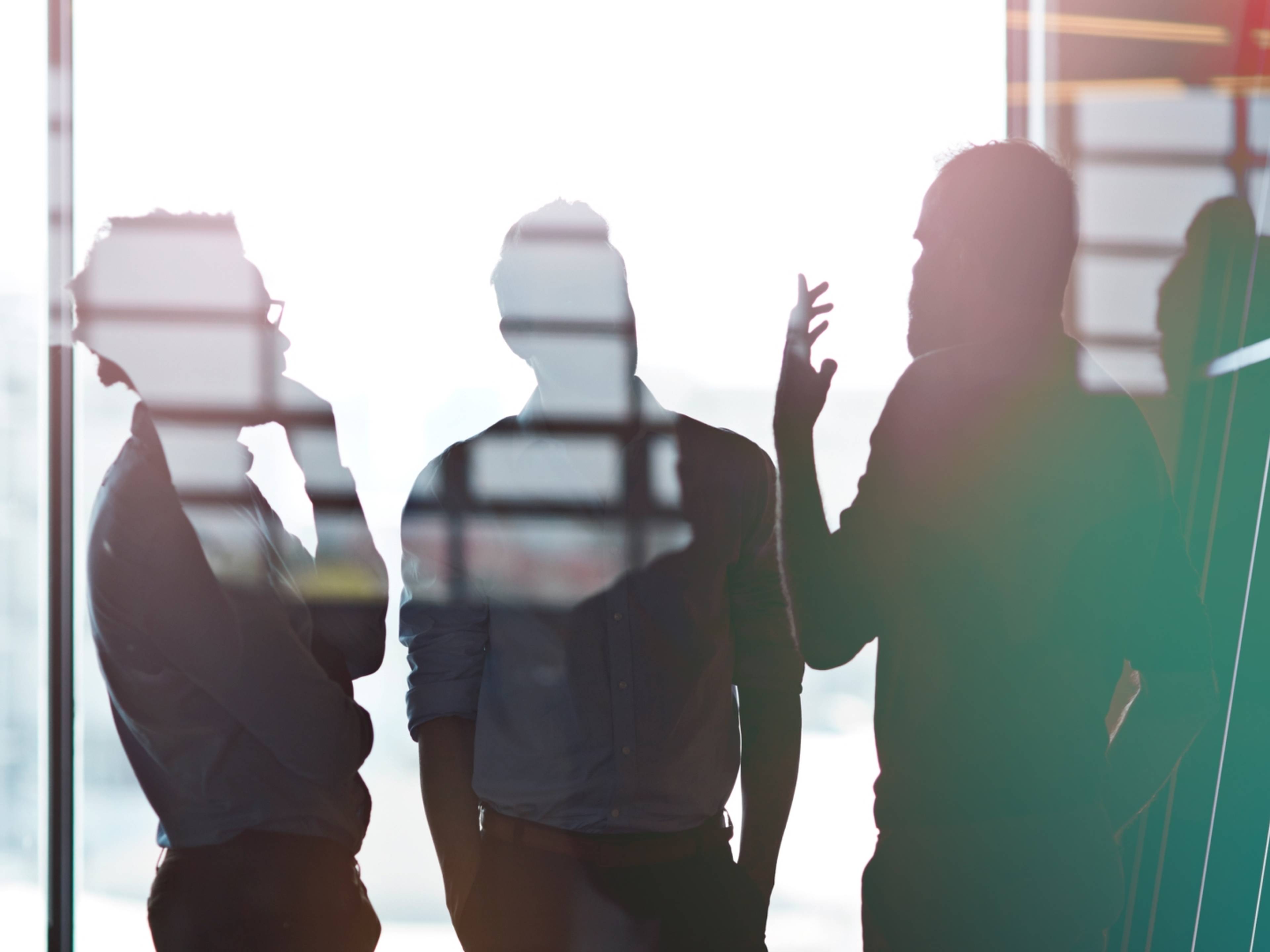 Silhouettes of three people engaged in conversation by a window
