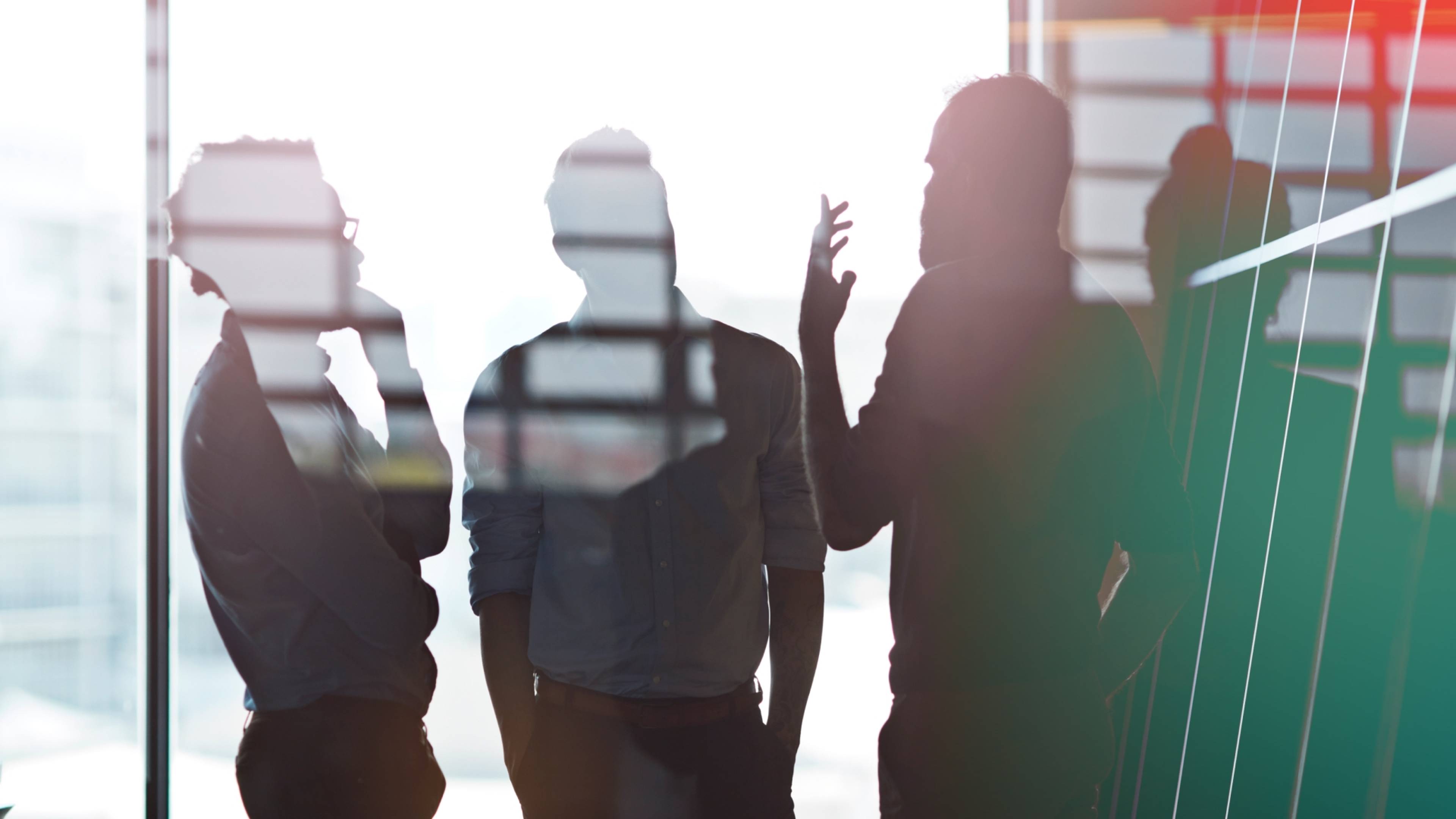 Silhouettes of three people engaged in conversation by a window