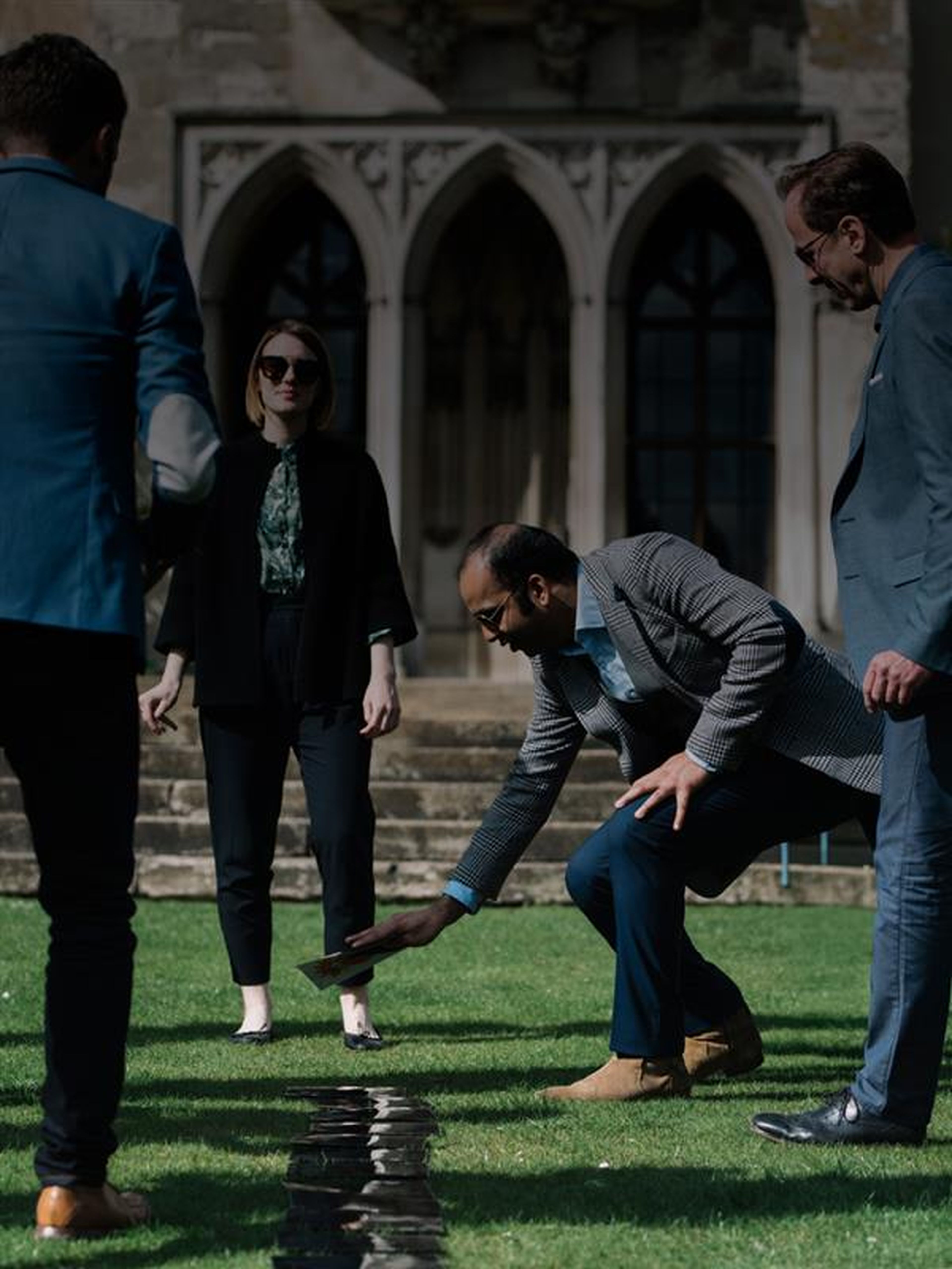 Four people in formal attire stand on grass near a historic building doing an experiential learning exercise