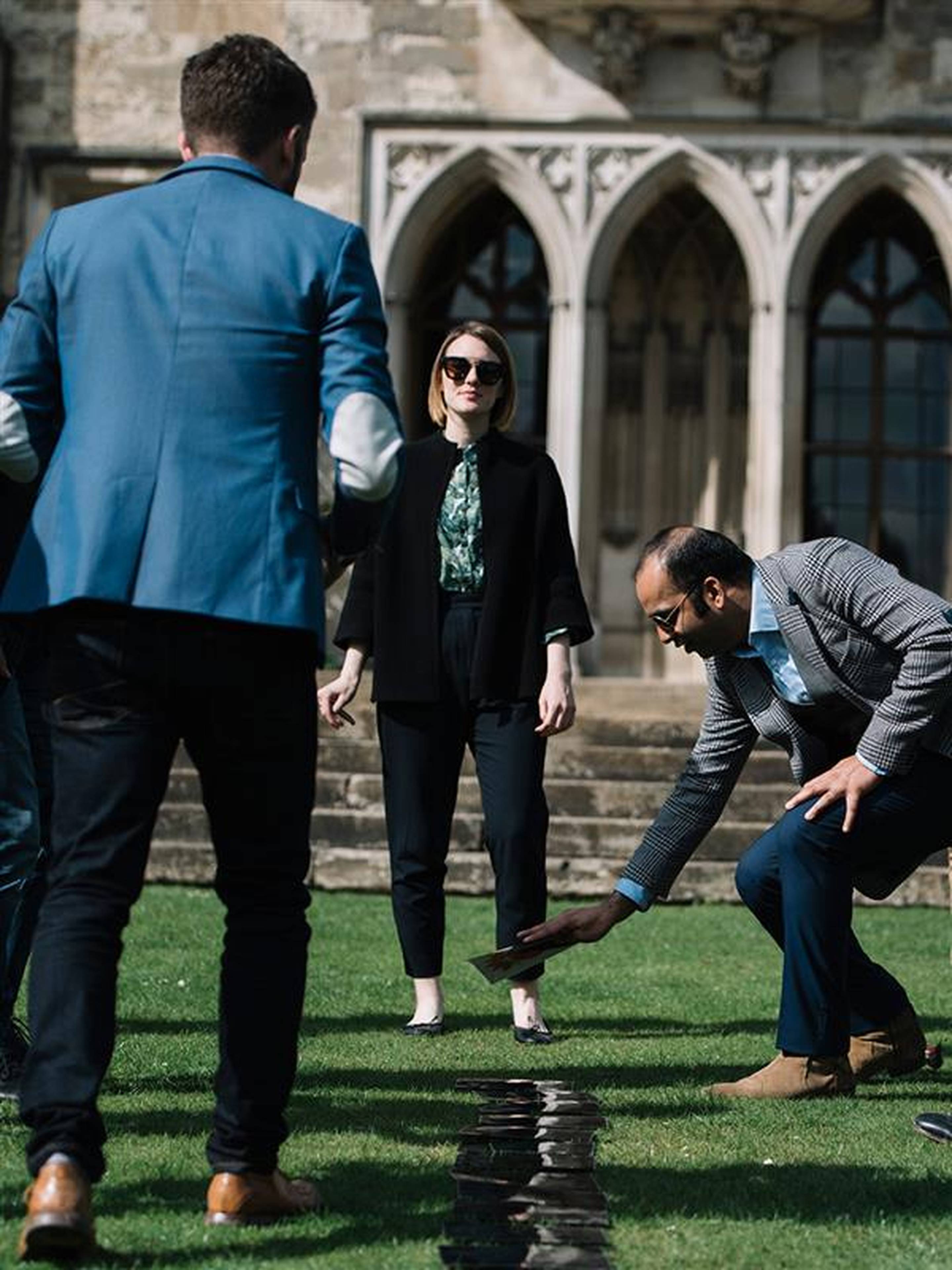People doing an experiential learning exercise on grass in front of a historic building with arched windows.