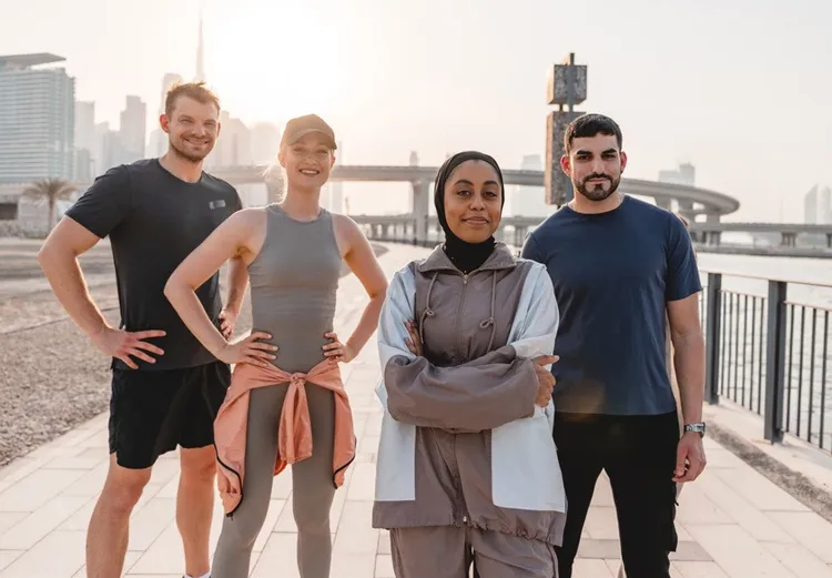 Four people in training gear on a Dubai waterfront promenade at sunrise
