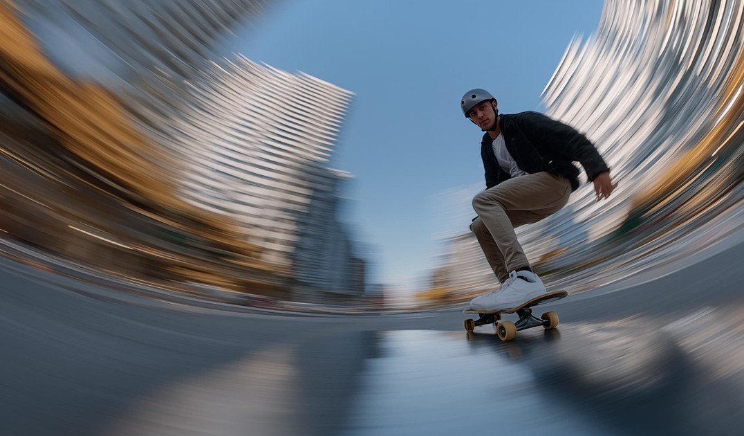 A person skateboards on a city street, creating a motion blur effect with tall buildings in the background.