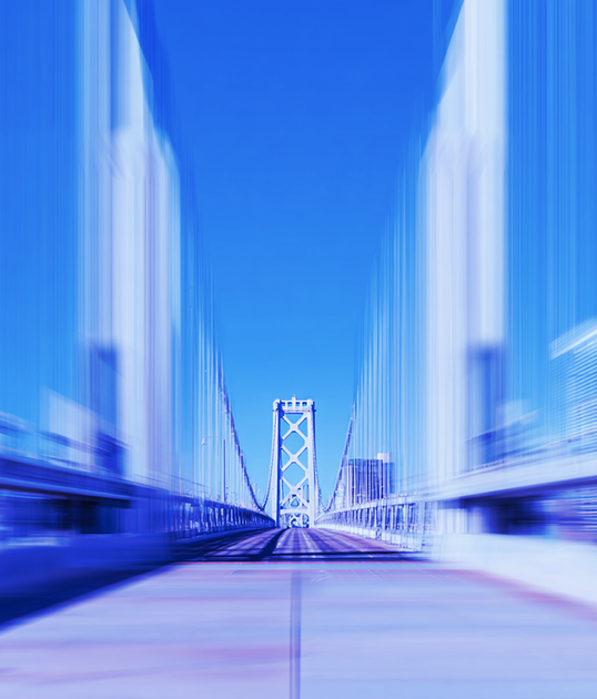 Person with short curly hair, wearing glasses and a blue coat, typing on a laptop against a solid blue background.