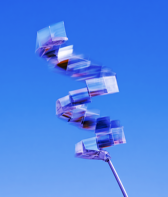 Three people in vibrant, flowing outfits walk dynamically against a teal backdrop, creating a blurred, motion effect.