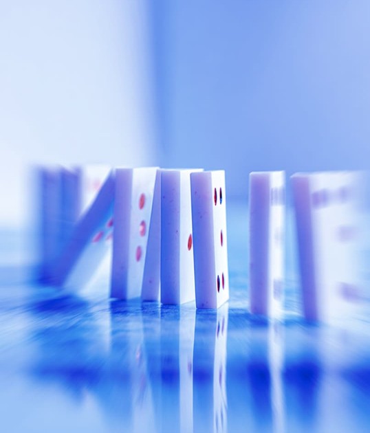 Close-up of dominoes in a line, captured in motion blur, creating a dynamic effect. The image is tinted with a blue hue.