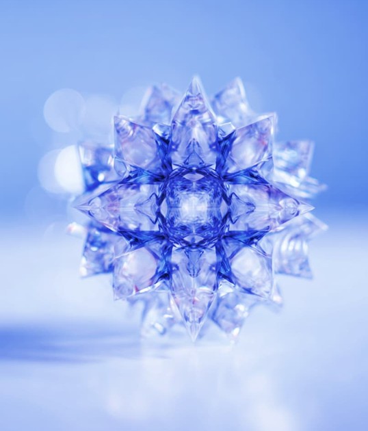 A crystal-like geometric star with multiple pointed facets, reflecting light in shades of blue, set against a soft blue background.