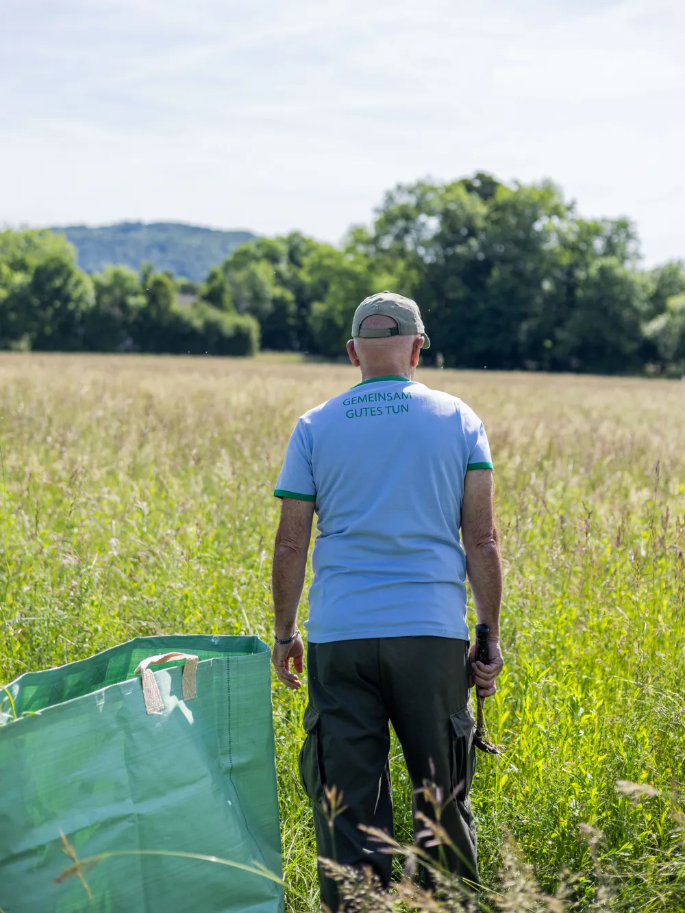 Mann sammelt Neophyten auf einer Wiese und trägt zu gemeinschaftlichem Einsatz für Umwelt und Landschaftsschutz bei