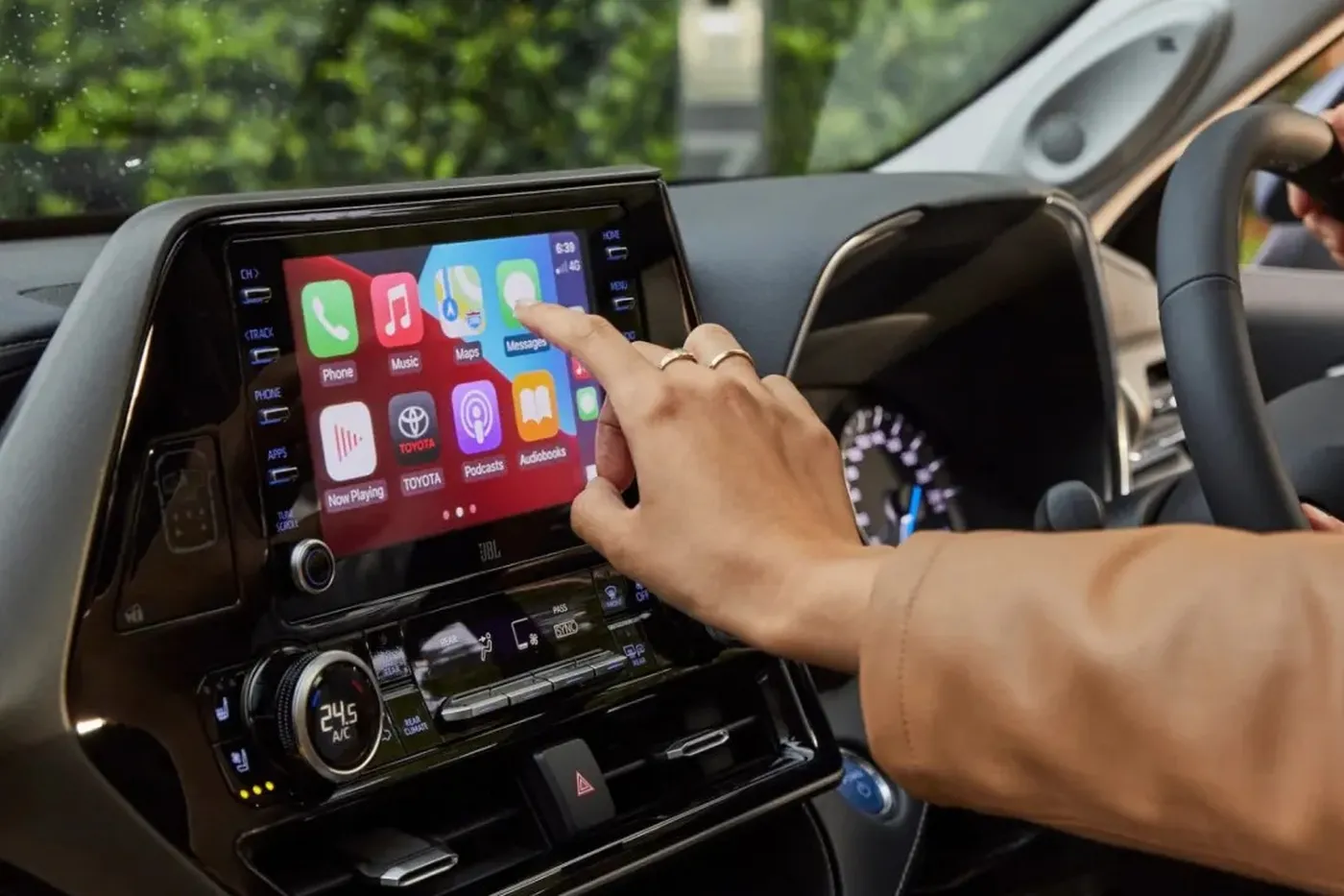 Close-up of a person using a car's touchscreen infotainment system displaying various app icons, with a hand reaching to tap the screen.