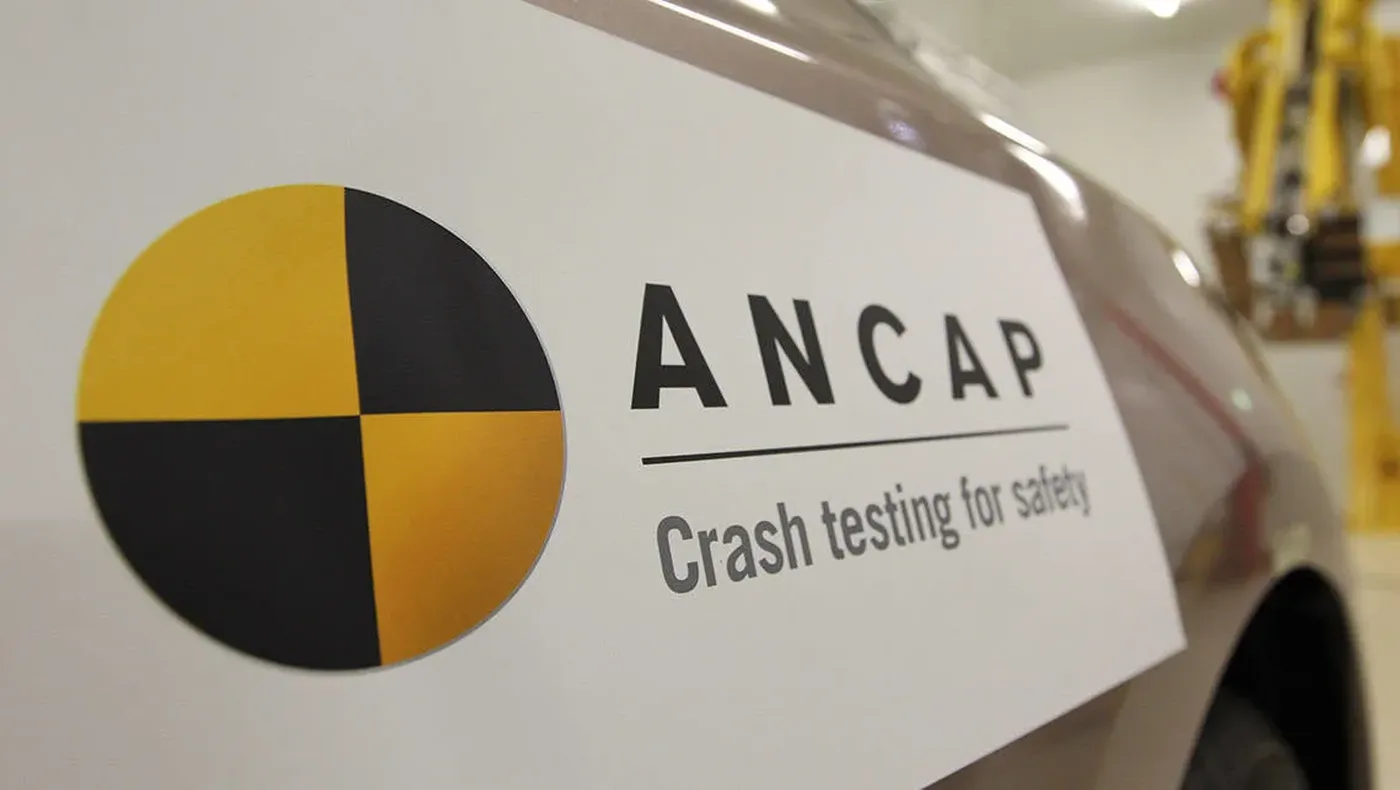 Close-up of a car with an ANCAP logo and the text "Crash testing for safety," featuring a yellow and black crash test symbol.