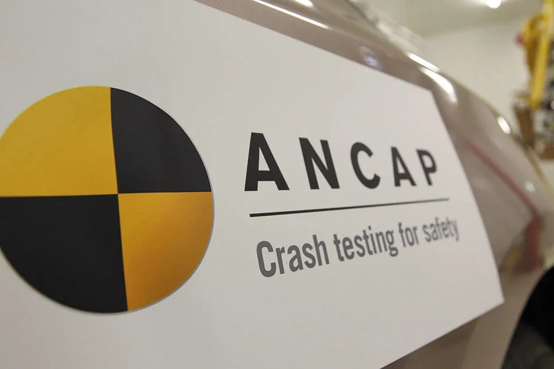 Close-up of a car with an ANCAP logo and the text "Crash testing for safety," featuring a yellow and black crash test symbol.