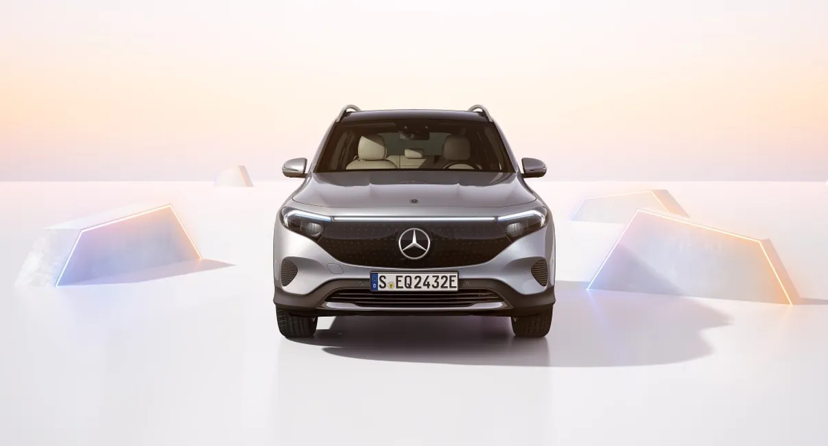 Front view of silver Mercedes electric SUV on a minimalist white set with pastel sunrise lighting and glowing geometric shapes