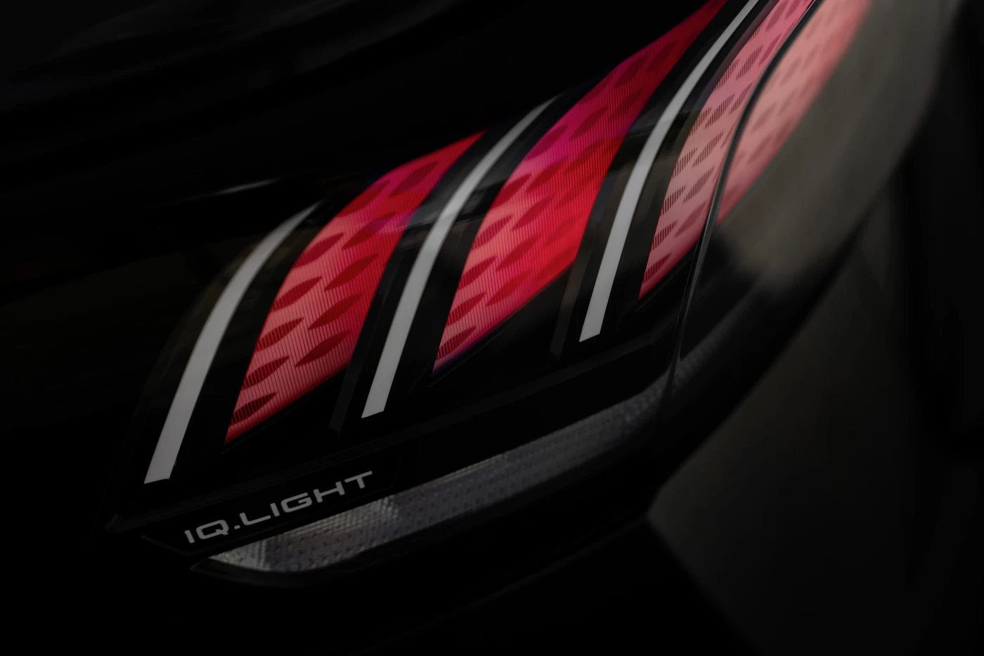 Close-up of a modern car taillight with sleek red LED patterns and "IQ.LIGHT" branding on a dark background.