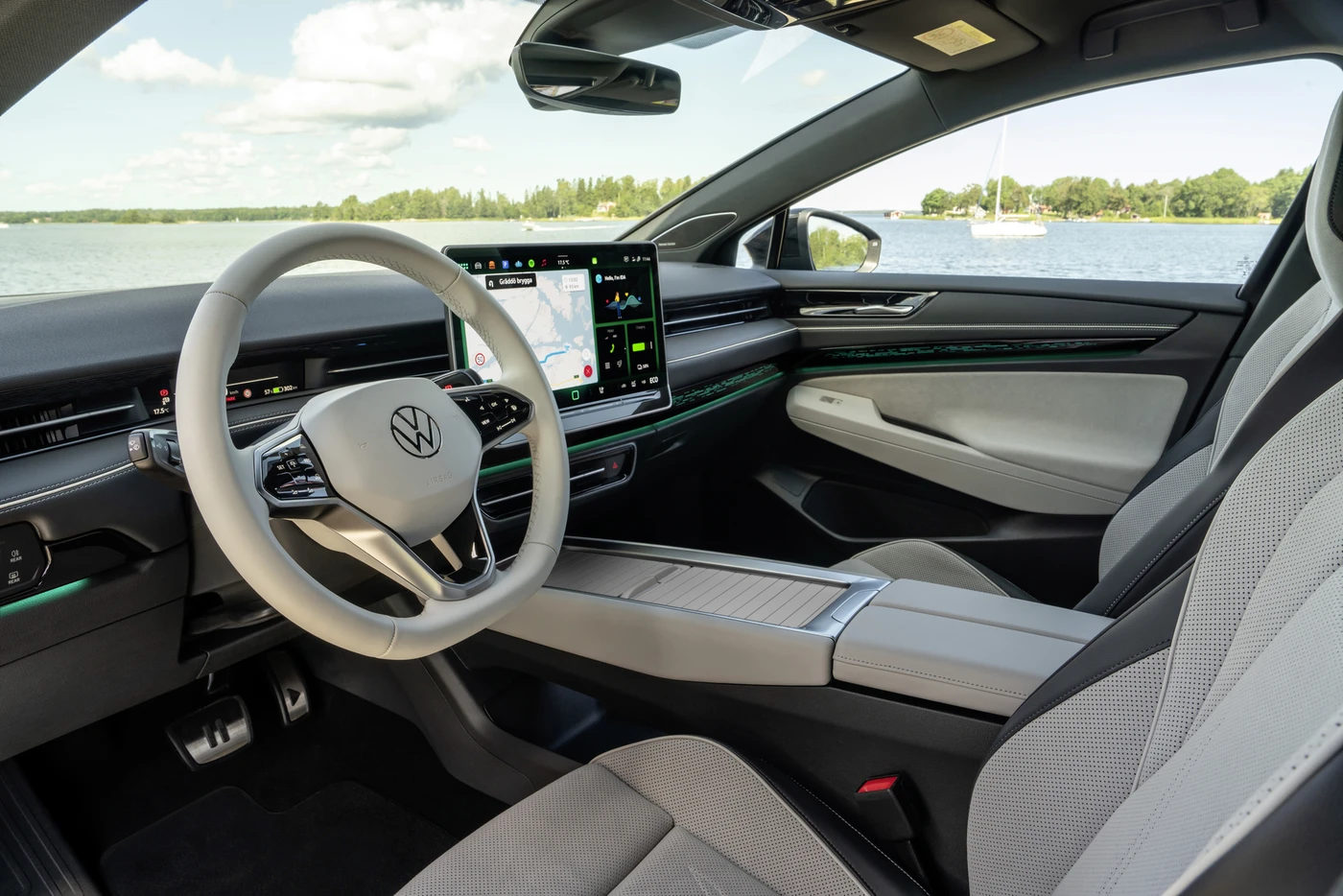 Modern car interior featuring a steering wheel, large touchscreen displaying navigation, and spacious seats with a lake view outside the window.