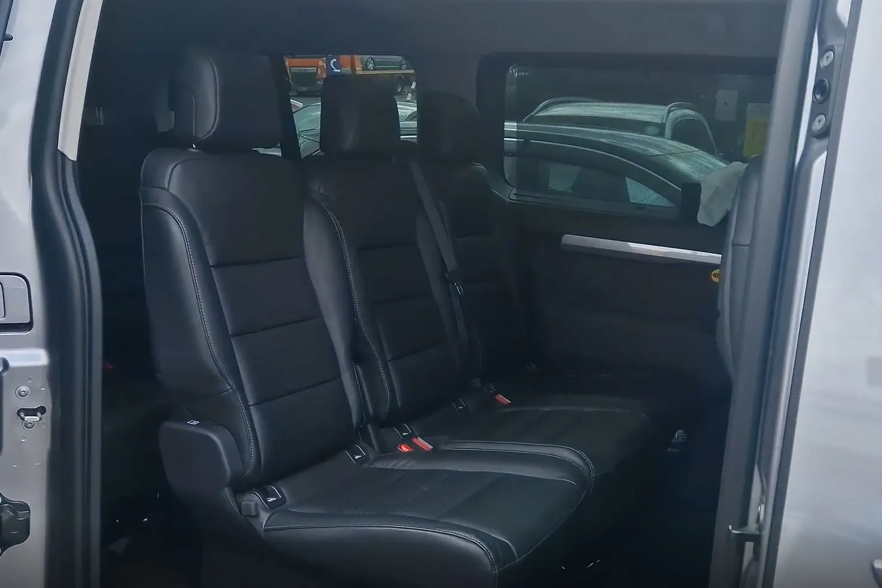 Interior of a vehicle showing three rows of black leather seats with an open sliding door on the right.