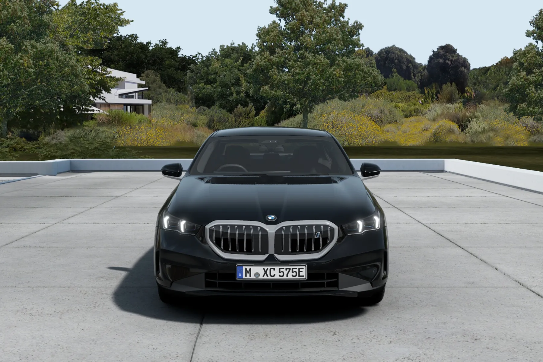 Front view of a black BMW sedan parked on a concrete driveway, with trees and greenery in the background.