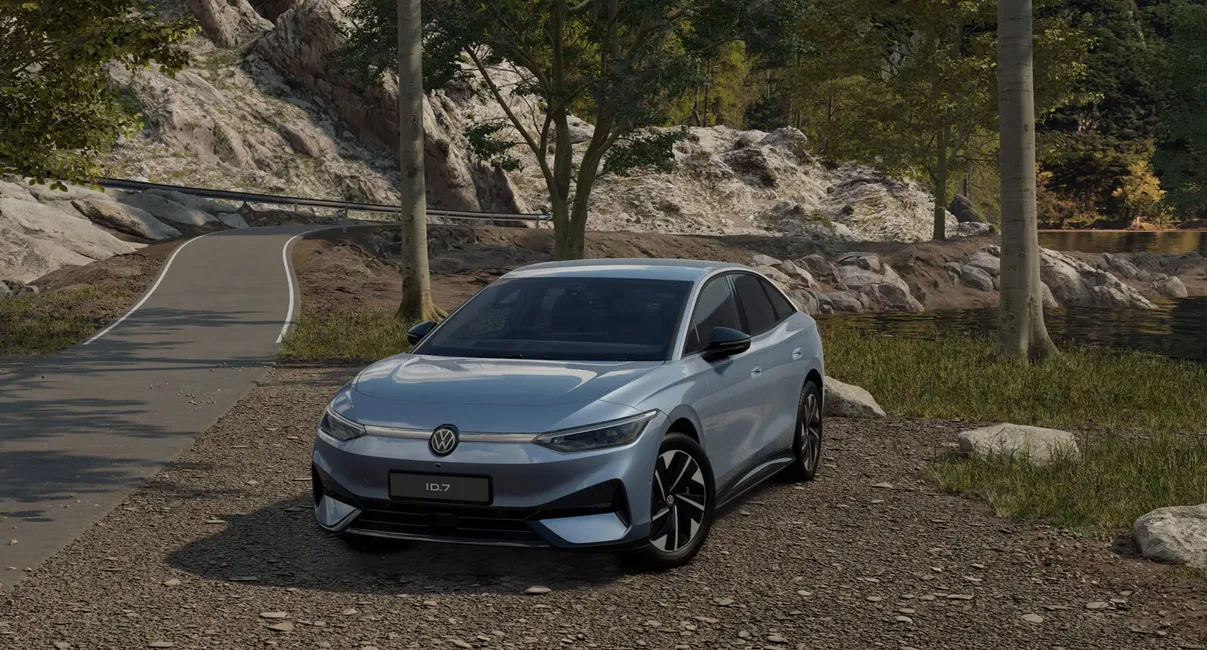 Silver car parked on a rocky path surrounded by trees and mountains, with a road curving nearby.