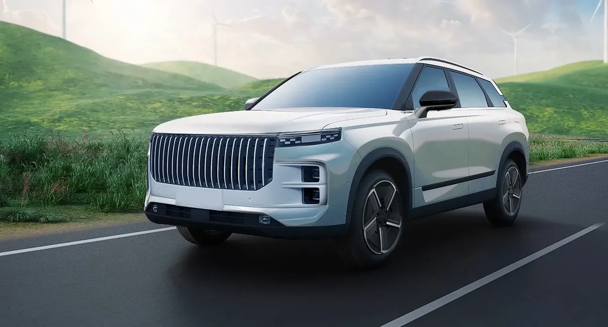 A sleek white SUV driving on a scenic road with green hills and wind turbines in the background under a partly cloudy sky.