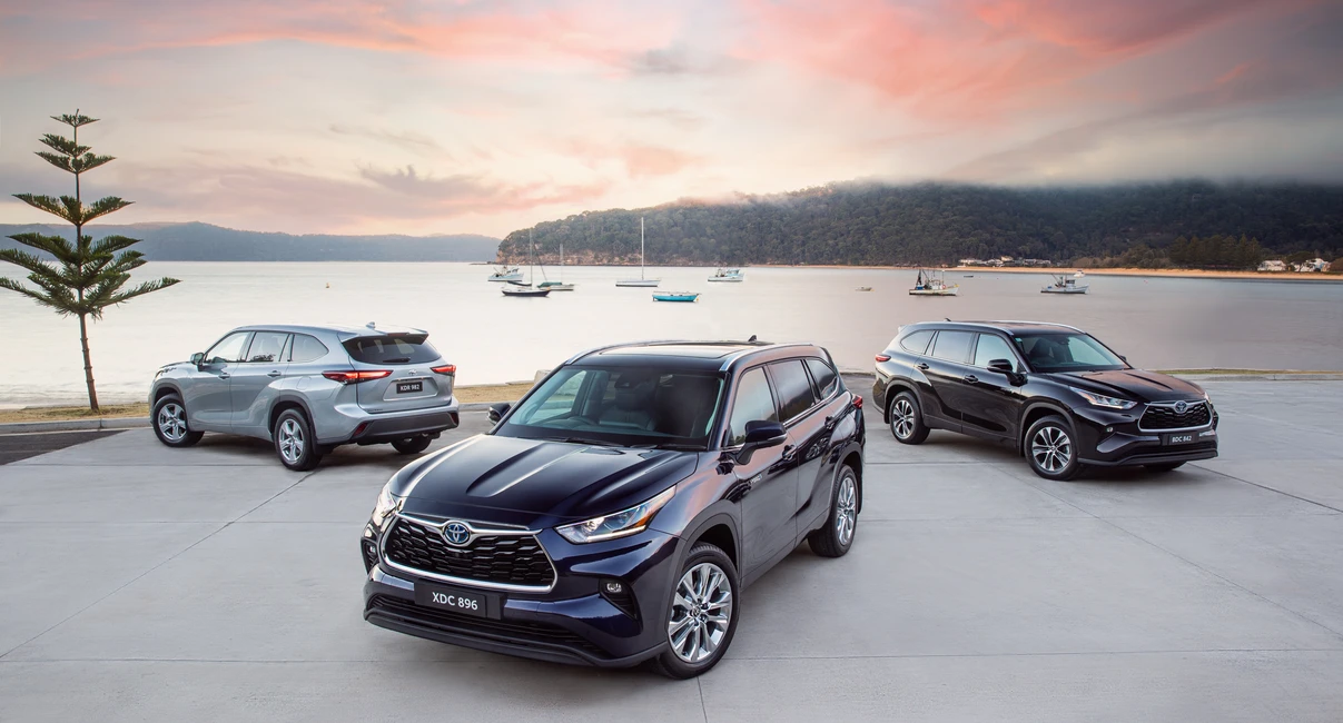 Three SUVs parked on a waterfront with a colorful sunset sky and boats in the background.