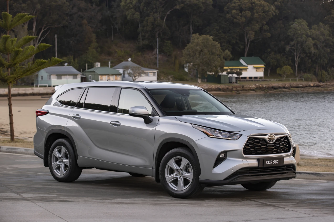 Silver SUV parked by a beachside road, with trees and small houses in the background on a cloudy day.