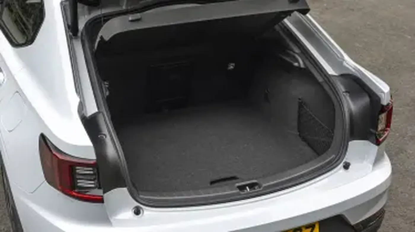 Open trunk of a white car showing a spacious, empty interior with dark carpeting, parked on a paved surface.
