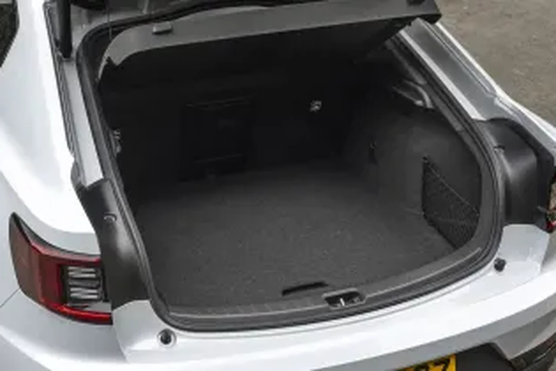 Open trunk of a white car showing a spacious, empty interior with dark carpeting, parked on a paved surface.