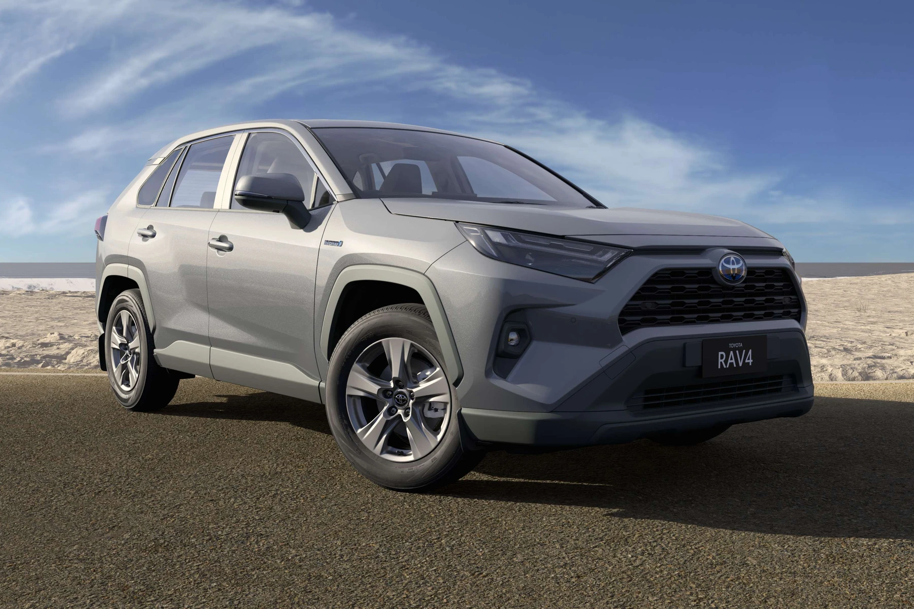 Silver Toyota RAV4 parked on a road by the beach under a clear blue sky.