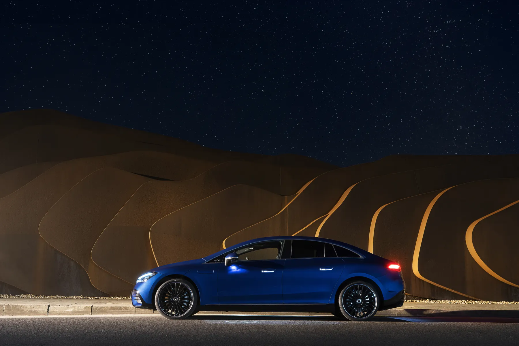 A blue car parked on a road at night, with illuminated starry sky in the background.