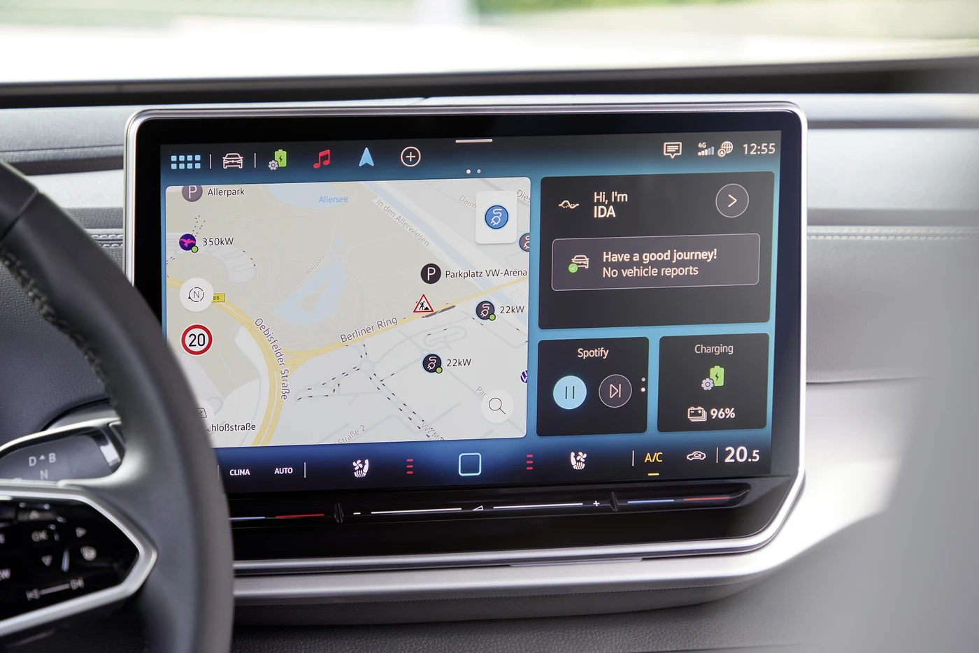 VW ID.4 EV dashboard display showing a navigation map, music player, messages, and battery status. Steering wheel visible on the left.