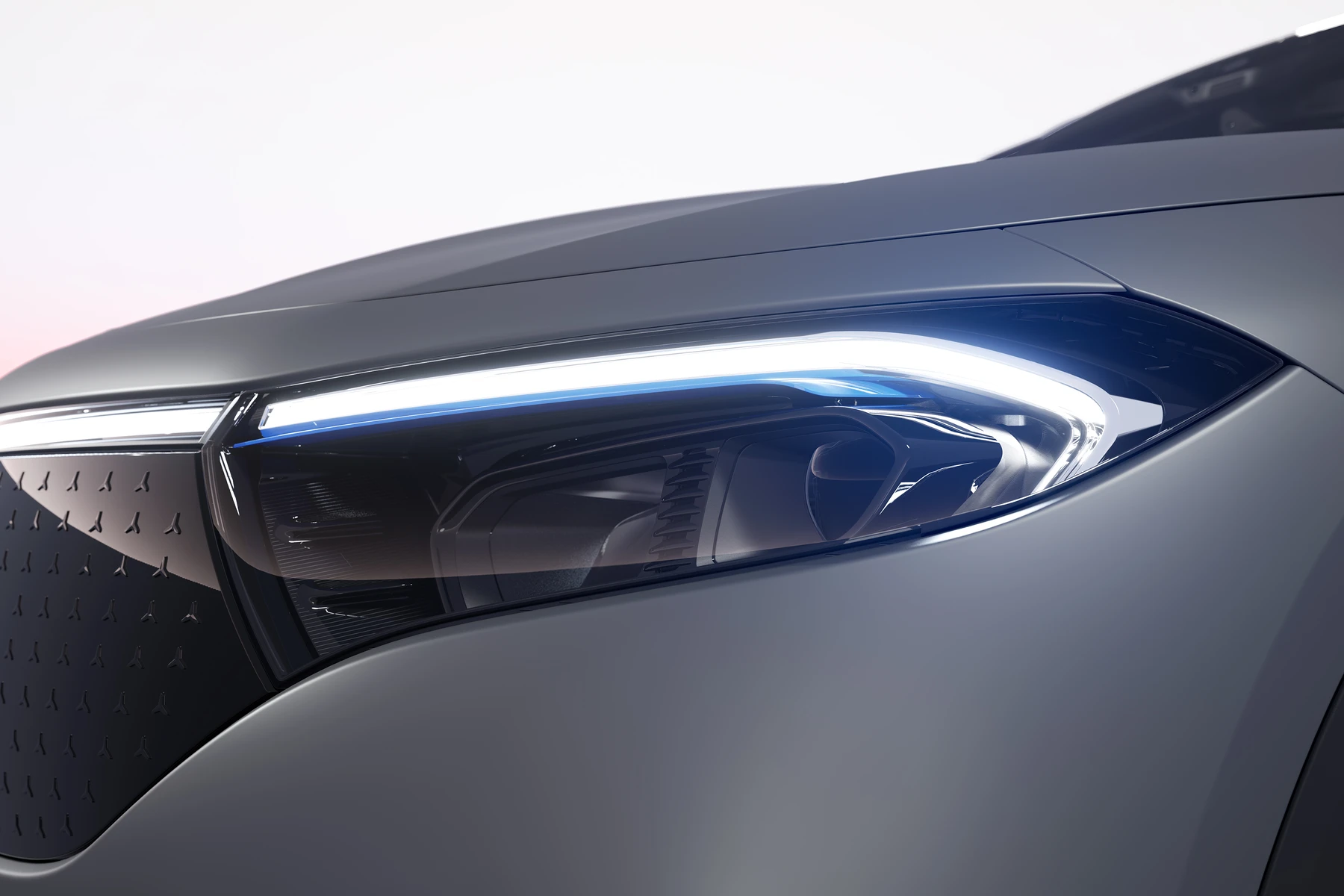 Close-up of a silver car's front end showing a sleek blue LED headlight and textured grille at dusk