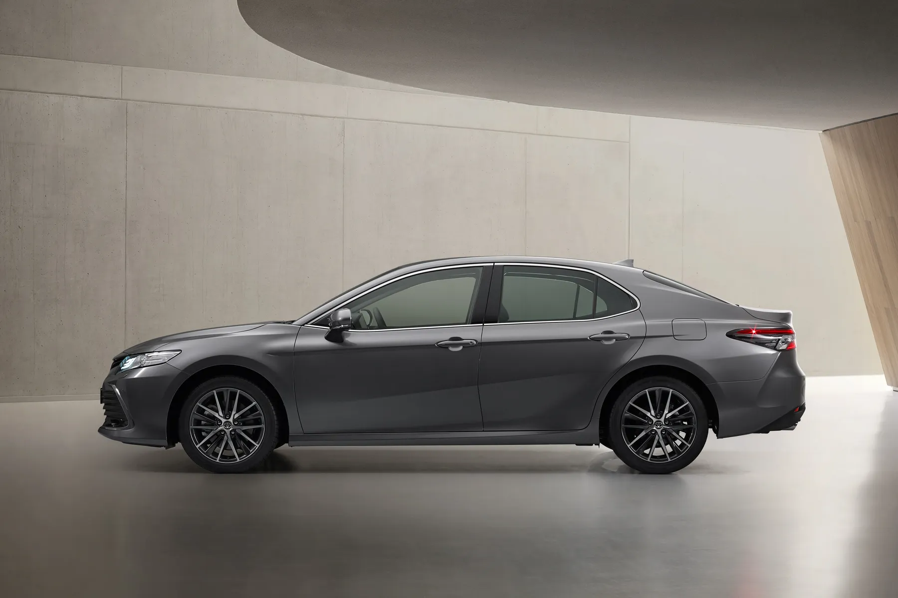 Sleek gray sedan parked indoors against a minimalist beige wall, showcasing its side profile and modern design.