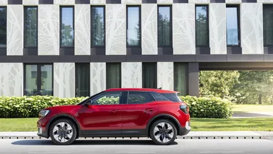 Red compact SUV parked on a street in front of a modern building with tall windows and a white tree-pattern facade.