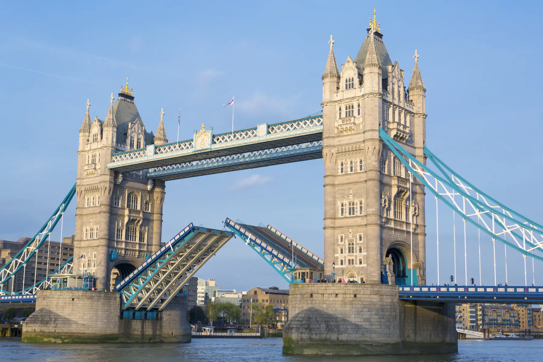Tower Bridge in London with its bascules raised over the River Thames under a clear blue sky.