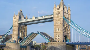 Tower Bridge in London with its bascules raised over the River Thames under a clear blue sky.