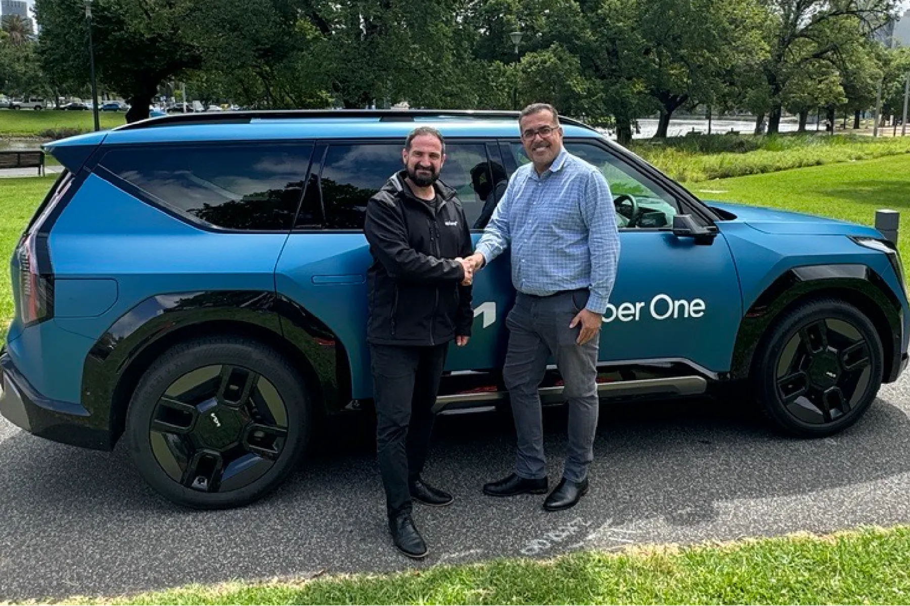Two men shaking hands in front of a blue Kia EV9