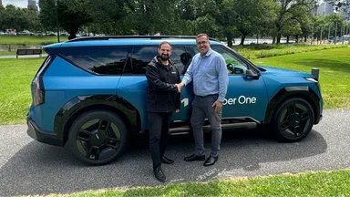 Two men shaking hands in front of a blue Kia EV9