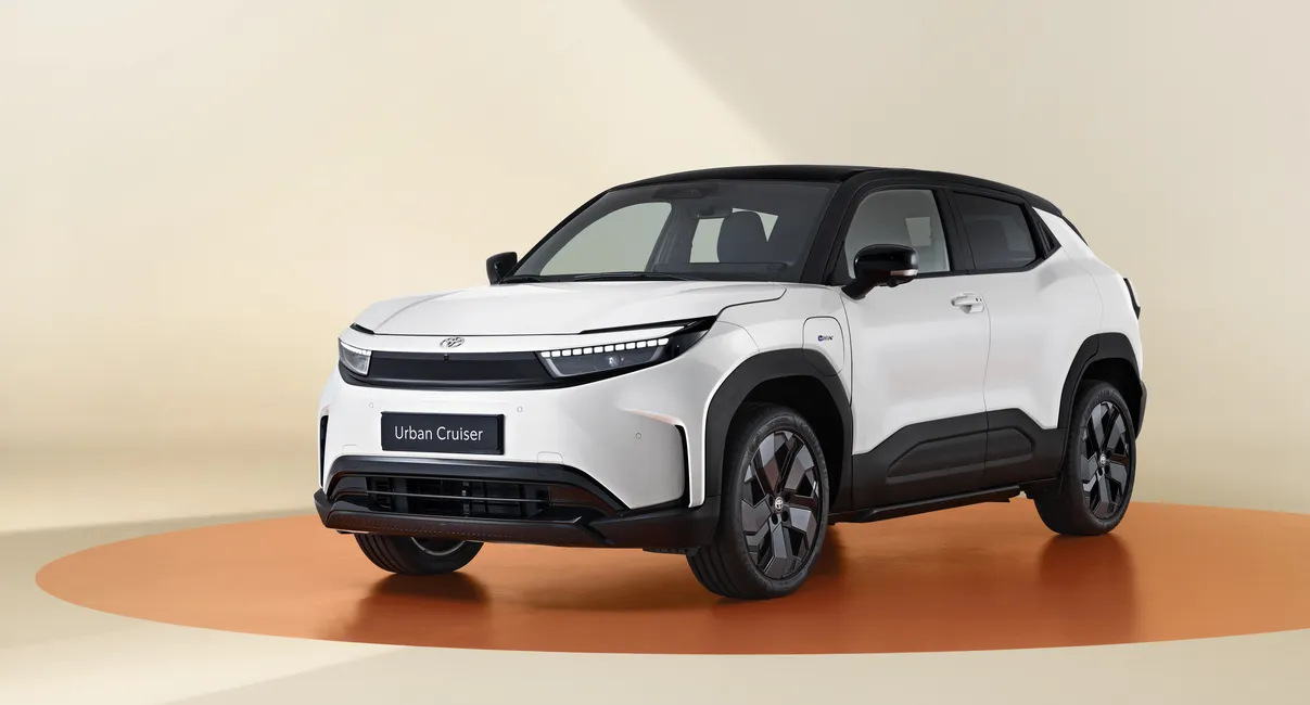 A modern, white SUV with a black roof and sleek design, displayed on an orange circular platform in a beige studio setting.