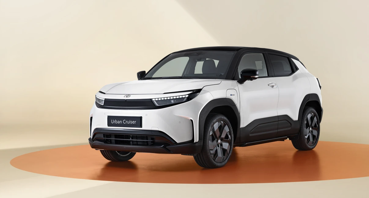 A modern, white SUV with a black roof and sleek design, displayed on an orange circular platform in a beige studio setting.