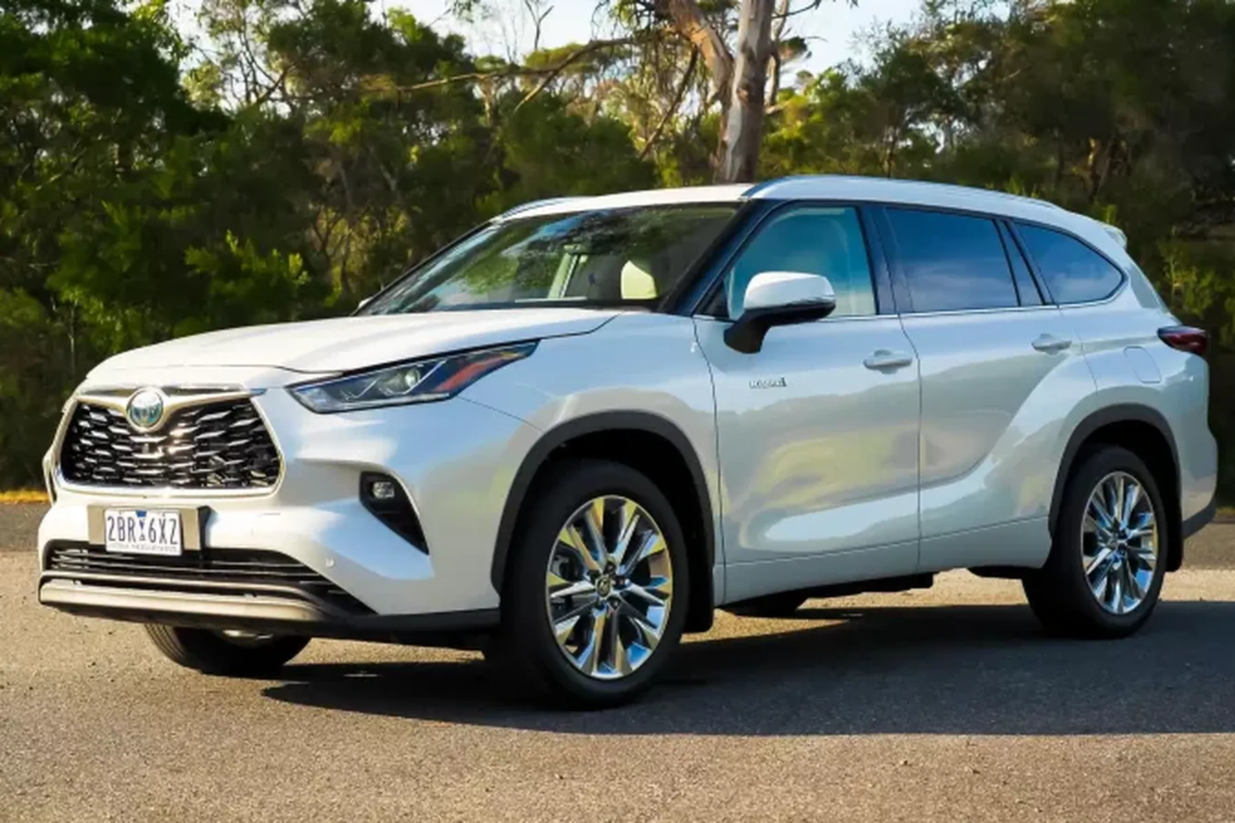 A white SUV parked on a paved road with trees in the background, featuring shiny chrome wheels and a sleek design.