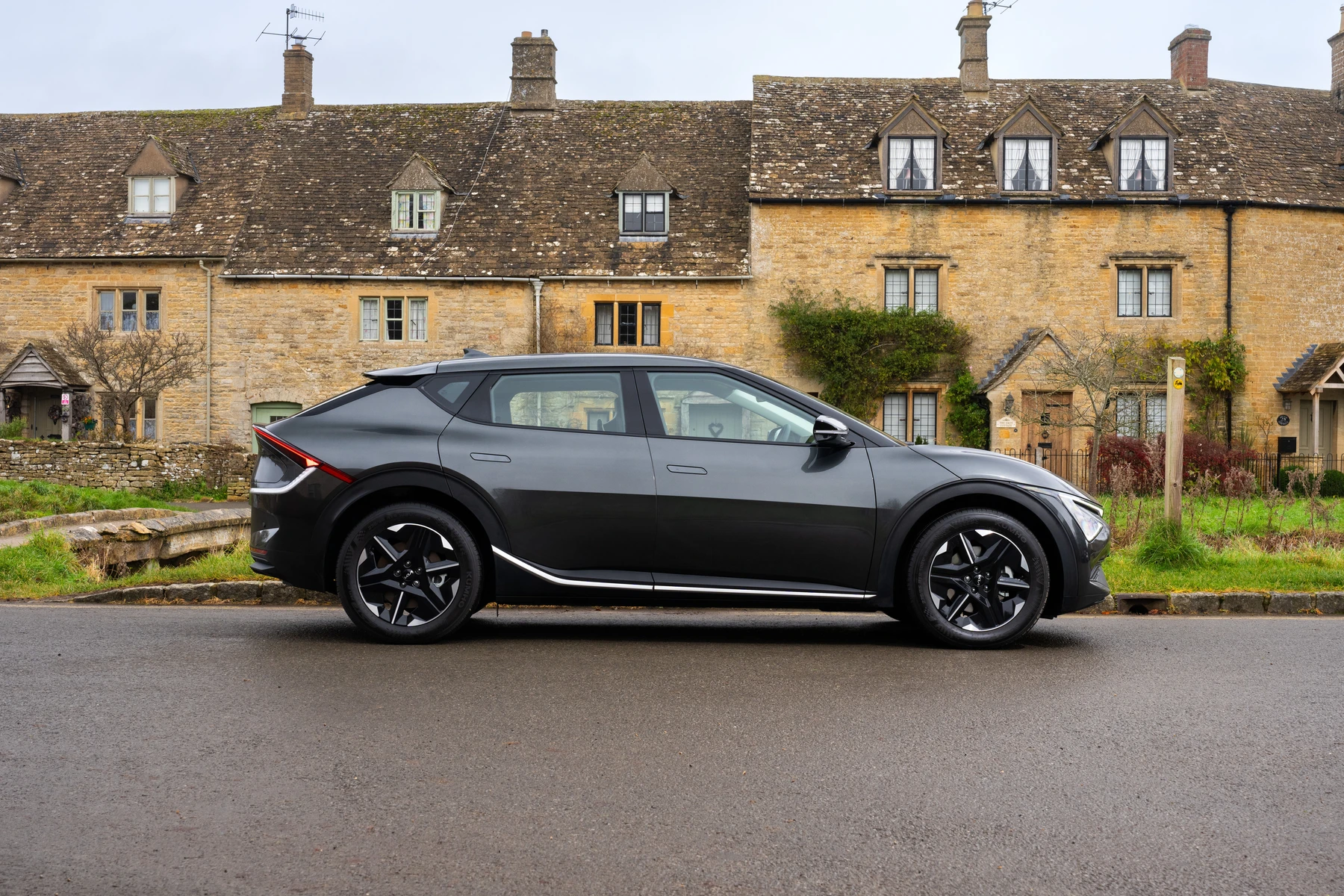 A sleek black Kia EV6 Air parked on a street in front of traditional stone houses with sloped roofs and chimneys.