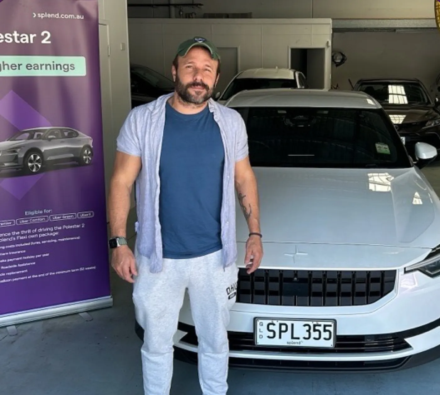 Man standing beside a white Polestar 2 car in a garage, with a promotional banner on the left.