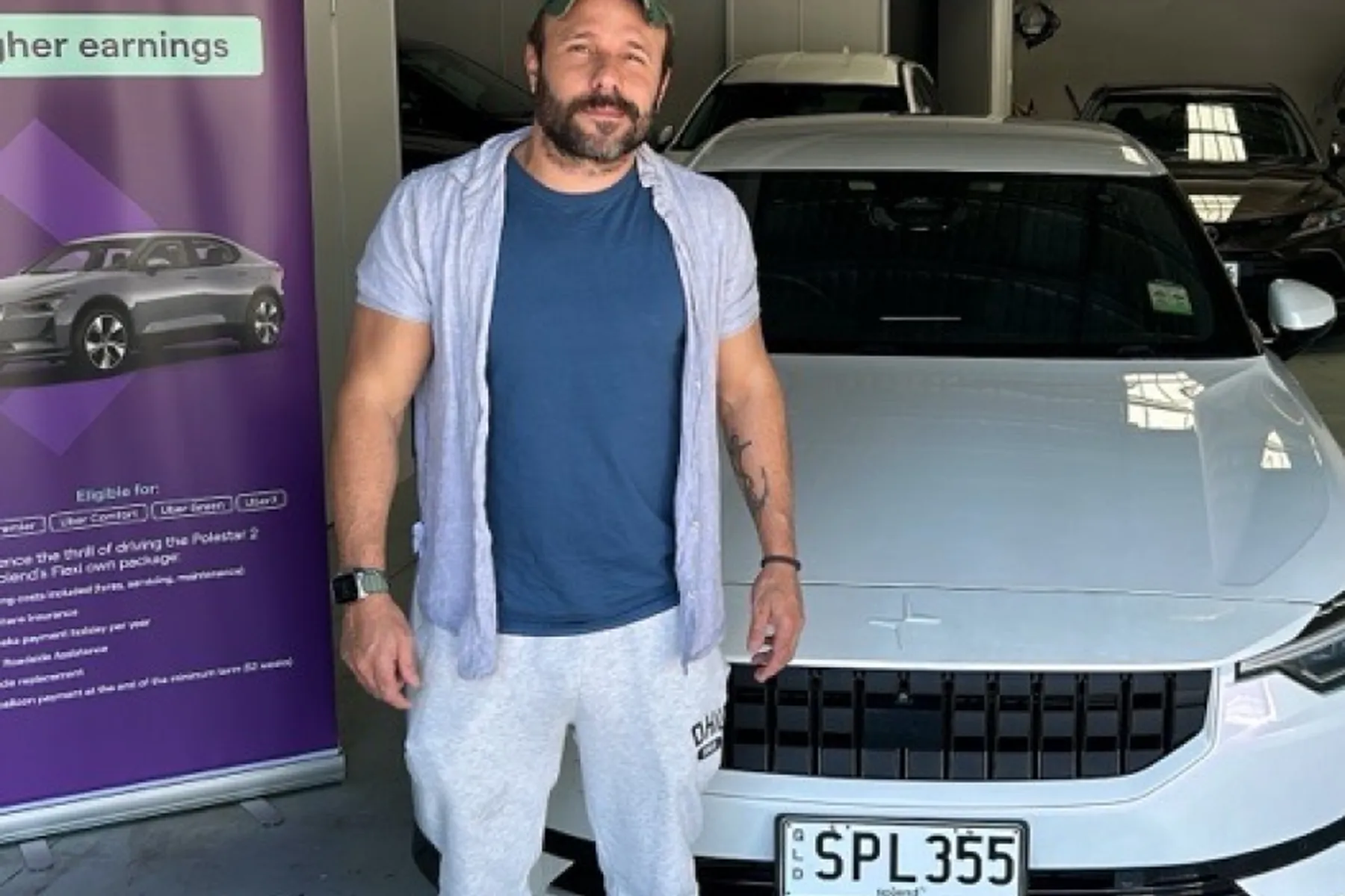 Man standing beside a white Polestar 2 car in a garage, with a promotional banner on the left.