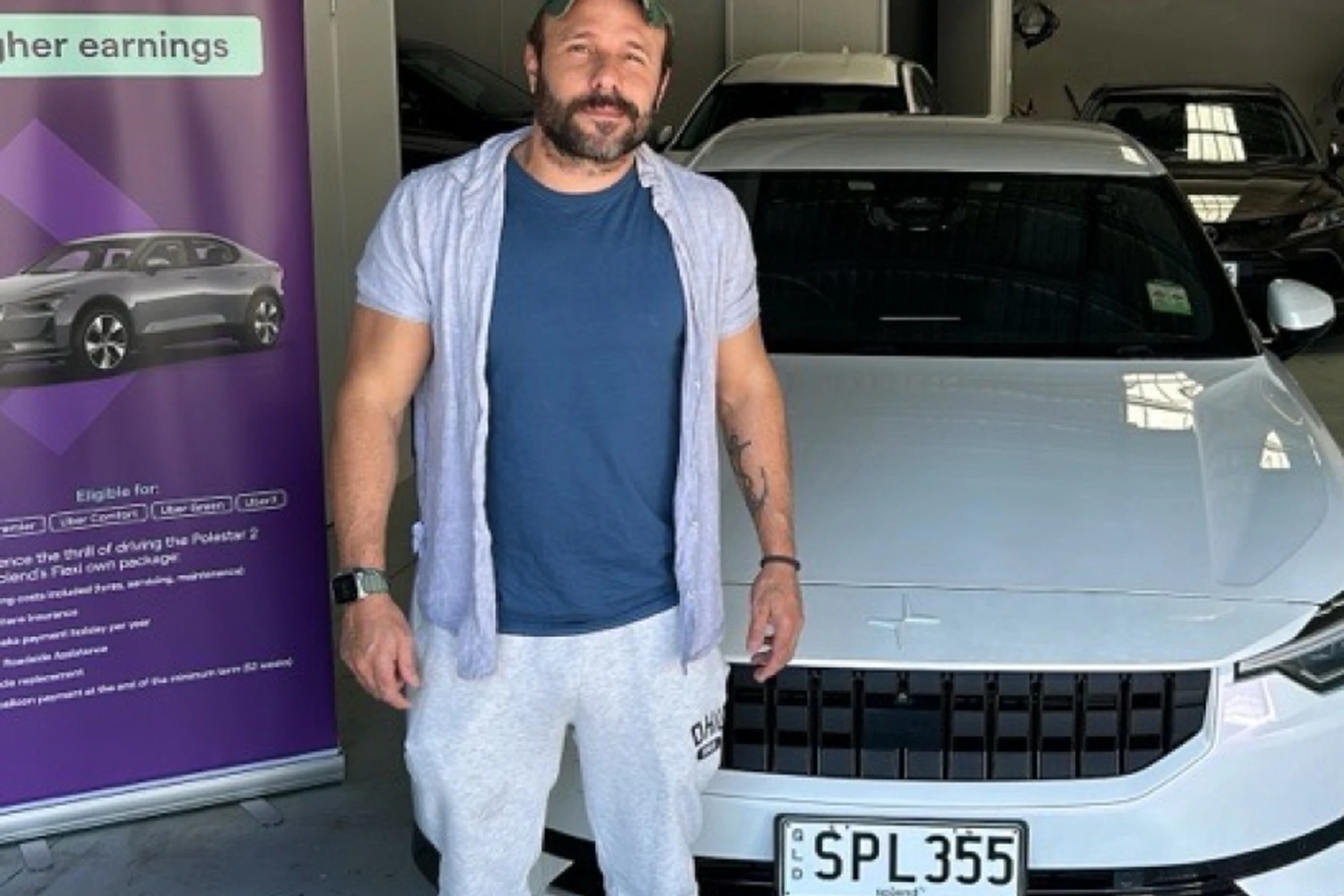 Man standing beside a white Polestar 2 car in a garage, with a promotional banner on the left.