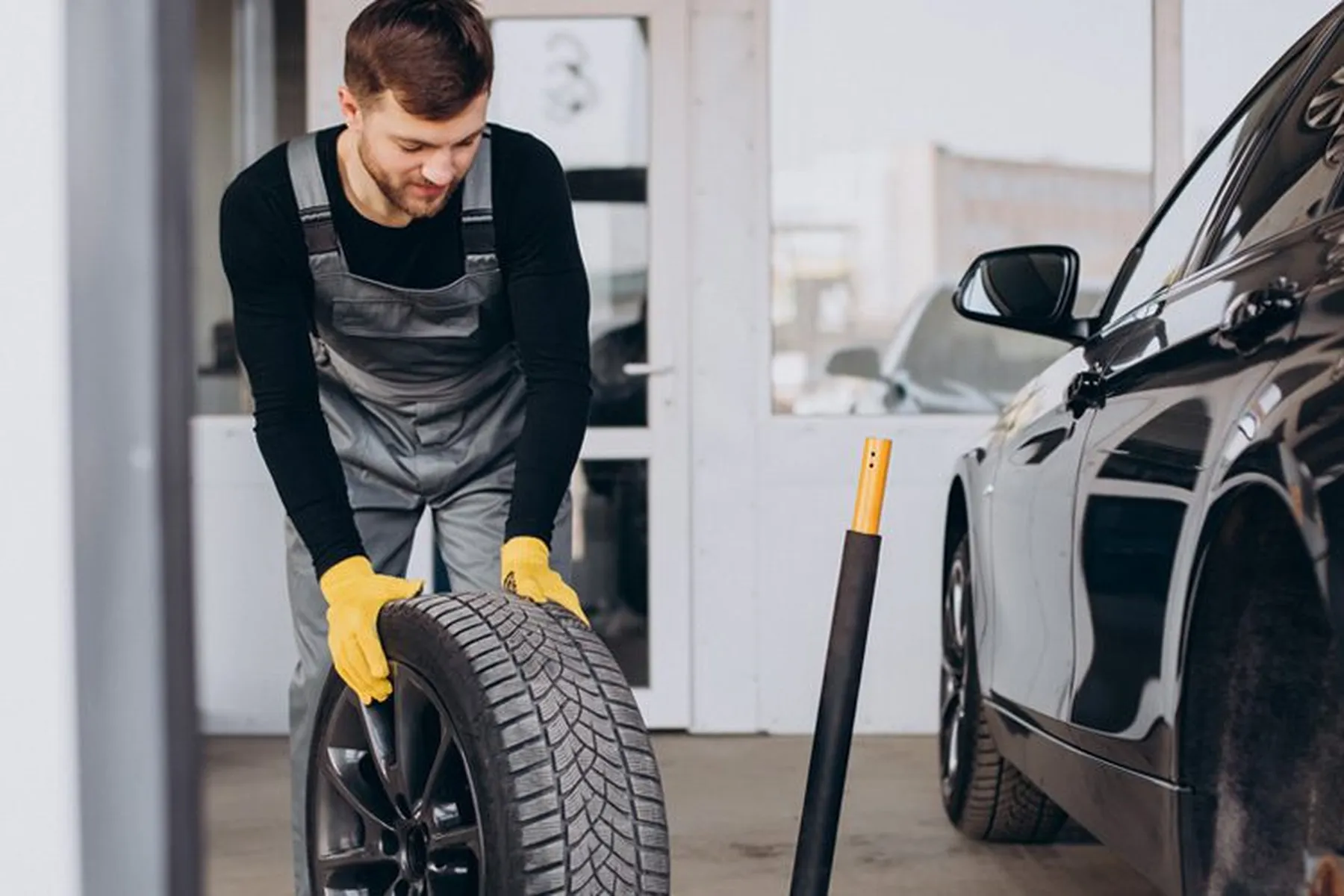 A mechanic rolling a tyre across a garage towards a black vehicle