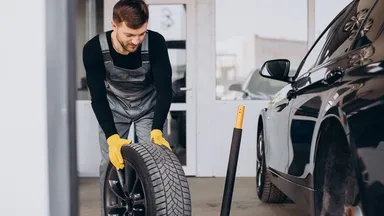 A mechanic rolling a tyre across a garage towards a black vehicle