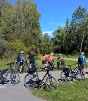 Eine Gruppe von Radfahrern hält mit ihren Fahrrädern an einem Rastplatz in einem von Bäumen umgebenen Gebiet an.